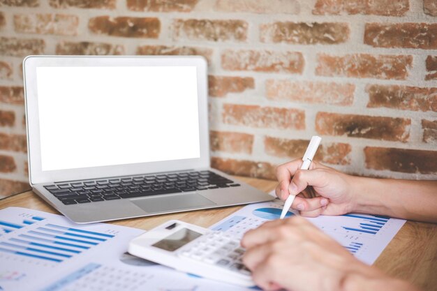 Sección media de hombres de negocios analizando el gráfico mientras usan la calculadora en la mesa en la oficina