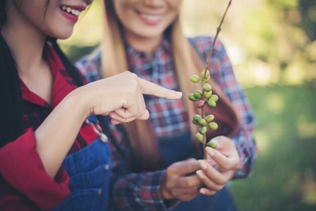 Sección media de una joven sonriente tocando una planta sostenida por un amigo