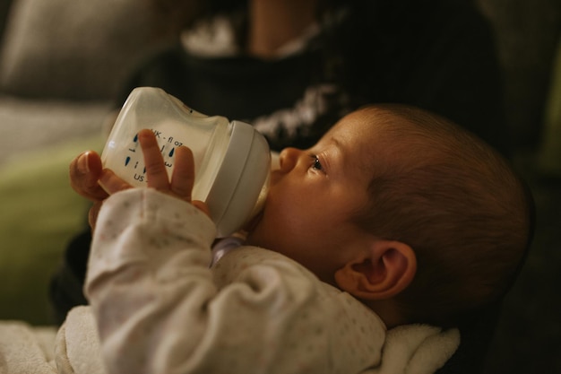 Foto sección media de una madre alimentando a su hija con una botella de leche en casa