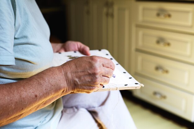 Sección media de las manos de las mujeres mayores haciendo trabajo de aguja en la cocina de su casa