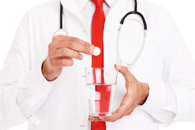 Una sección media de un médico sosteniendo una pastilla y un vaso de agua