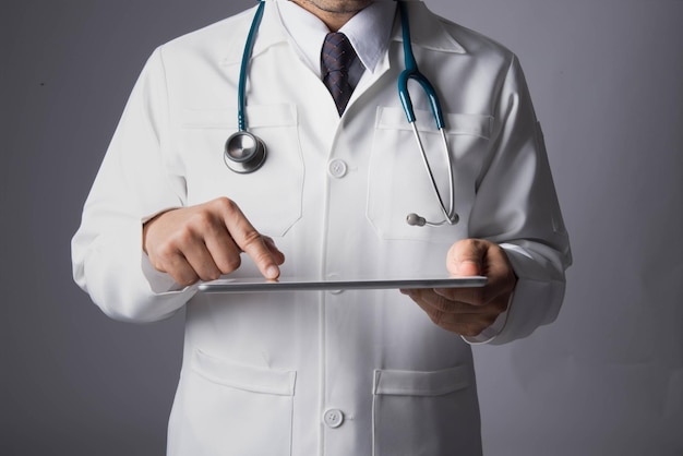 Sección media del médico usando una tableta digital contra un fondo gris
