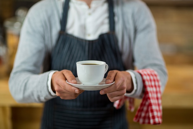 Foto sección media del mesero de pie con una taza de café