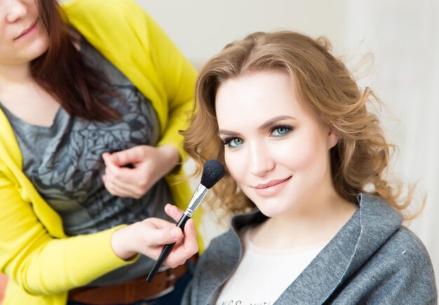 Sección media de una mujer aplicando maquillaje con pincel en la cara de una amiga