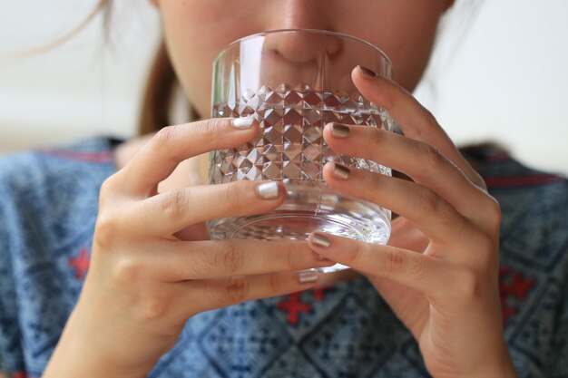 Foto sección media de una mujer bebiendo agua de un vaso en casa