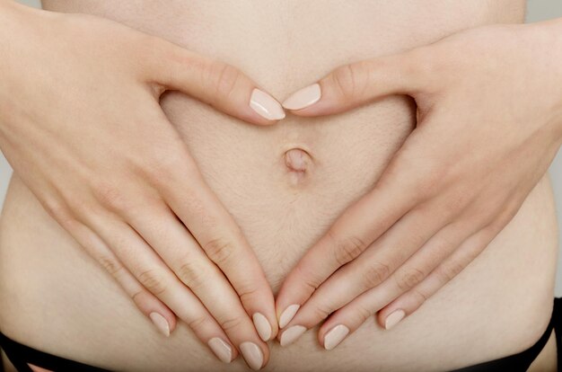 Foto sección media de una mujer sin camisa haciendo forma de corazón en su vientre