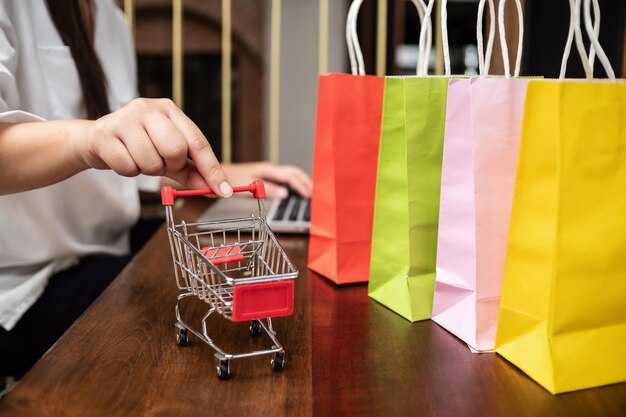 Sección media de una mujer con carrito de compras y bolsas en la mesa