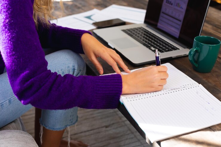 Foto sección media de una mujer caucásica usando una computadora portátil y escribiendo notas en una mesa de café trabajando en casa. negocios, vida doméstica, positividad y trabajo remoto.