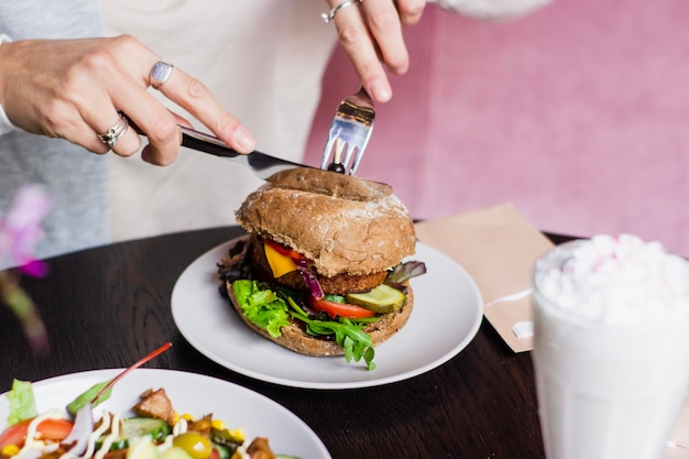 Sección media de una mujer comiendo una hamburguesa en la mesa