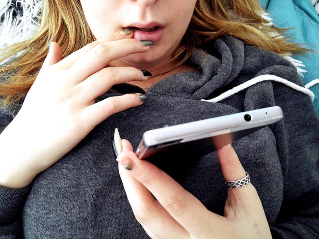 Foto sección media de una mujer con el dedo en la boca usando el teléfono