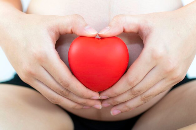 Foto sección media de una mujer embarazada con forma de corazón rojo