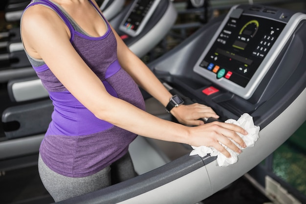 Foto sección media de la mujer embarazada que limpia la cinta de correr en el gimnasio