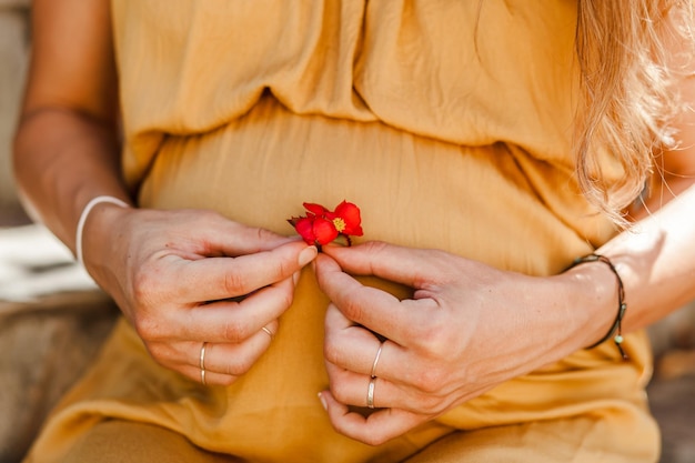 Foto sección media de una mujer embarazada sosteniendo una flor mientras está sentada al aire libre