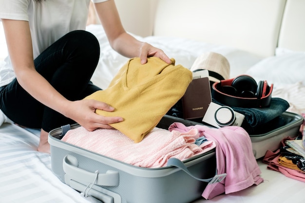 Sección media de una mujer empacando un suéter en una maleta en casa