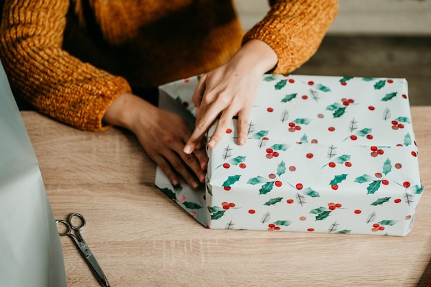 Foto sección media de una mujer envolviendo el regalo de navidad por la mesa