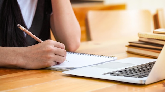 Sección media de una mujer escribiendo en un libro en el escritorio