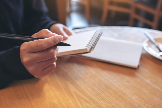 Foto sección media de una mujer escribiendo en un libro mientras está sentada en la mesa