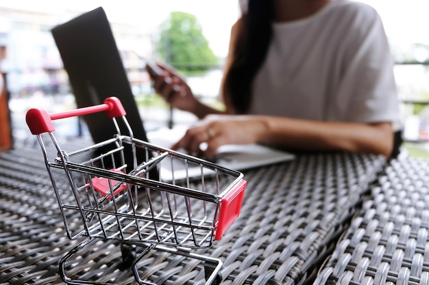 Foto sección media de una mujer haciendo compras en línea con un carrito en primer plano