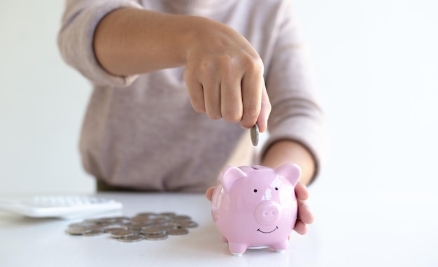 Foto sección media de una mujer insertando una moneda en la alcancía en la mesa