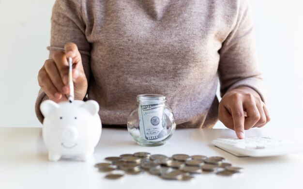 Foto sección media de una mujer insertando papel moneda en la alcancía en la mesa