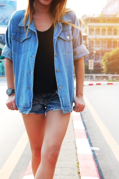 Foto sección media de una mujer joven con chaqueta de vaqueros y pantalones calientes de pie en la calle de la ciudad