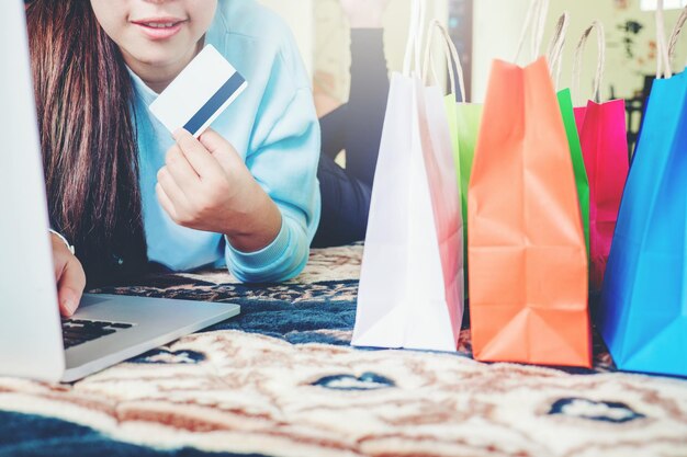 Sección media de una mujer joven haciendo compras en línea mientras está acostada en la cama en casa