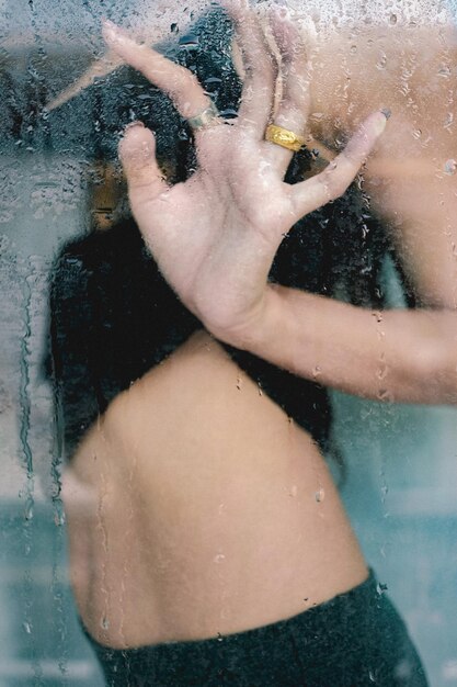Foto sección media de una mujer joven de pie detrás de una ventana de vidrio húmedo