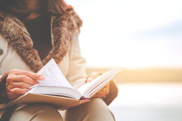 Foto sección media de una mujer leyendo un libro contra el lago