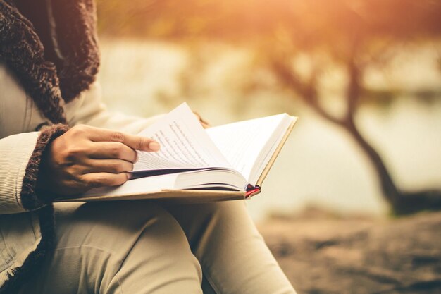 Sección media de una mujer leyendo un libro mientras está sentada al aire libre