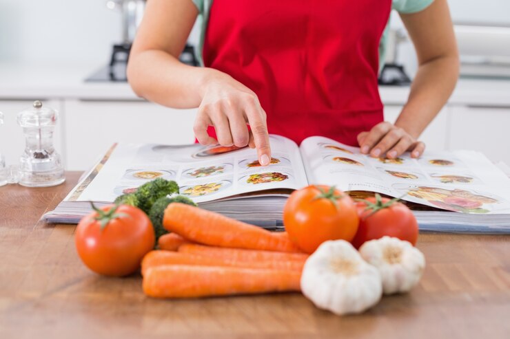 Foto sección media de una mujer con libro de recetas y verduras