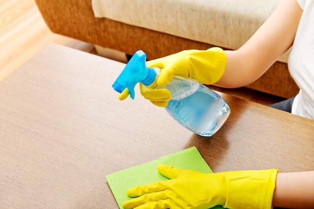 Sección media de una mujer limpiando una mesa de madera en casa