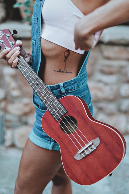 Foto sección media de una mujer mostrando un tatuaje mientras sostiene una guitarra