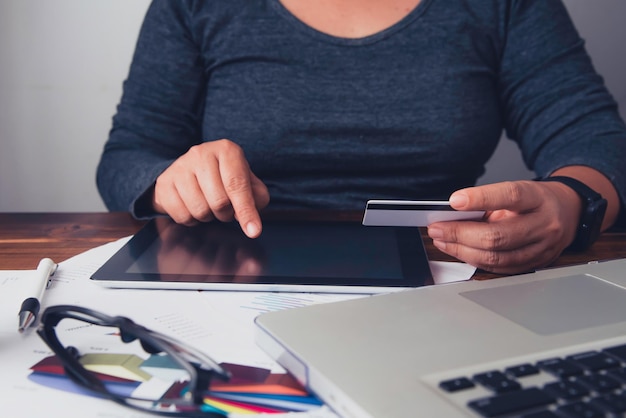 Foto sección media de una mujer de negocios con una tarjeta de crédito mientras usa una tableta digital en la mesa