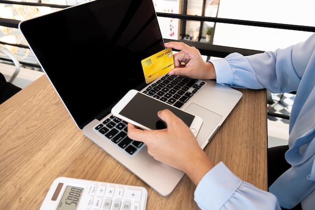 Sección media de una mujer de negocios con una tarjeta de crédito mientras usa tecnologías en el escritorio