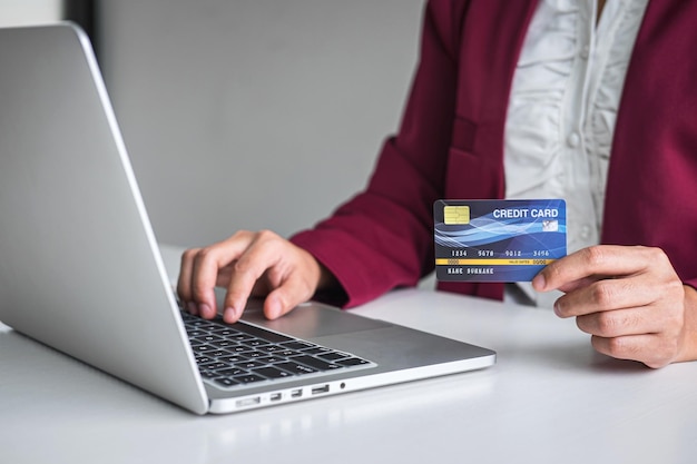 Sección media de una mujer de negocios con tarjeta de crédito usando una computadora portátil en el escritorio de la oficina