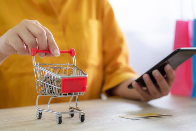 Foto sección media de una mujer con pequeñas compras mientras usa el teléfono en la mesa