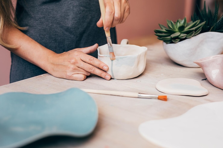 Foto sección media de una mujer pintando una jarra en el escritorio