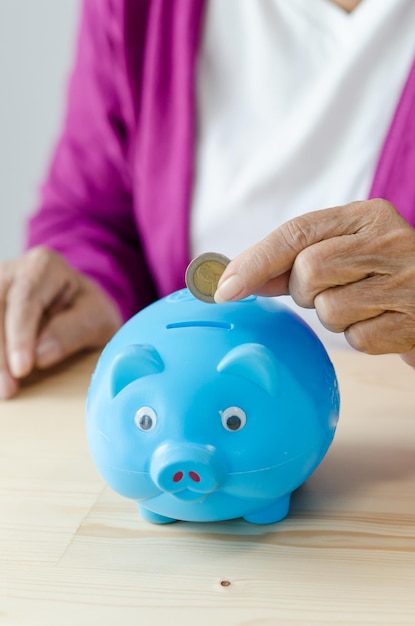 Foto sección media de una mujer poniendo una moneda en la alcancía en la mesa