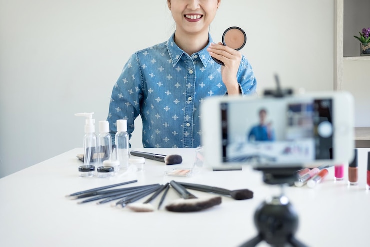 Foto sección media de una mujer con productos de belleza grabando video a través de un teléfono móvil