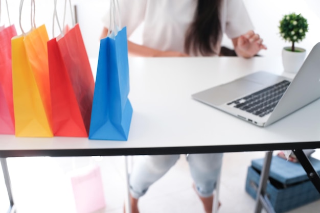 Sección media de una mujer sentada con bolsas de compras coloridas en la mesa