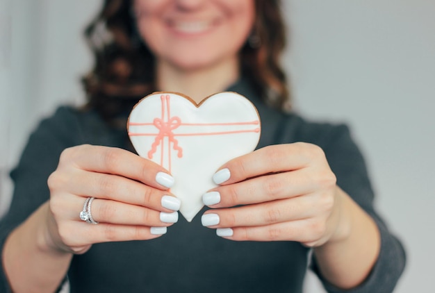 Foto sección media de una mujer sonriente sosteniendo una galleta en forma de corazón en casa