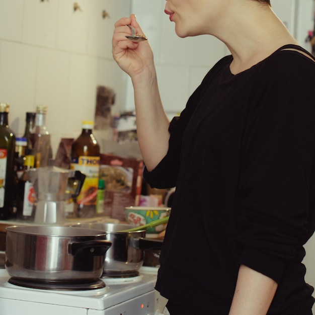 Foto sección media de una mujer soplando una cuchara mientras prepara comida en casa