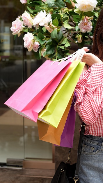 Foto sección media de una mujer sosteniendo bolsas de compras mientras está de pie junto a plantas rosadas en flor