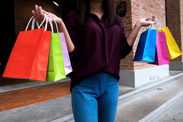 Sección media de una mujer sosteniendo bolsas de compras de varios colores en la acera