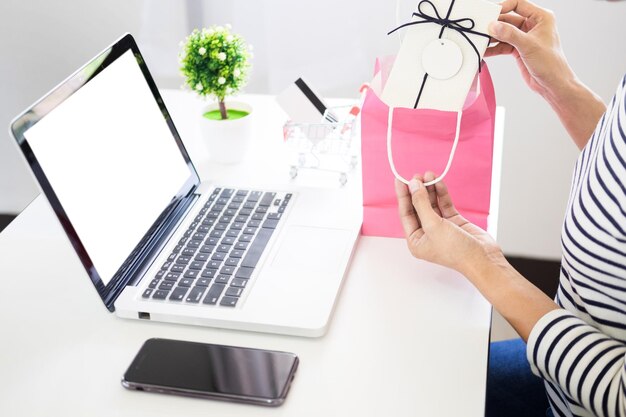 Sección media de una mujer sosteniendo una caja de regalos con una computadora portátil y un teléfono en el escritorio