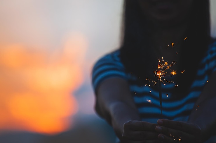Foto sección media de una mujer sosteniendo una chispa durante la puesta de sol