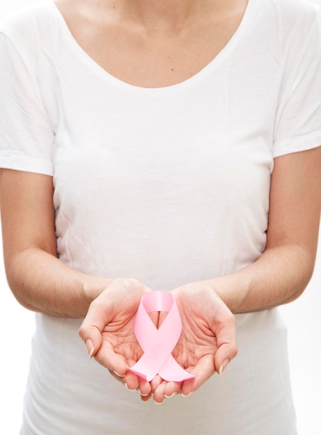 Foto sección media de una mujer sosteniendo una cinta de concienciación sobre el cáncer de mama contra un fondo blanco