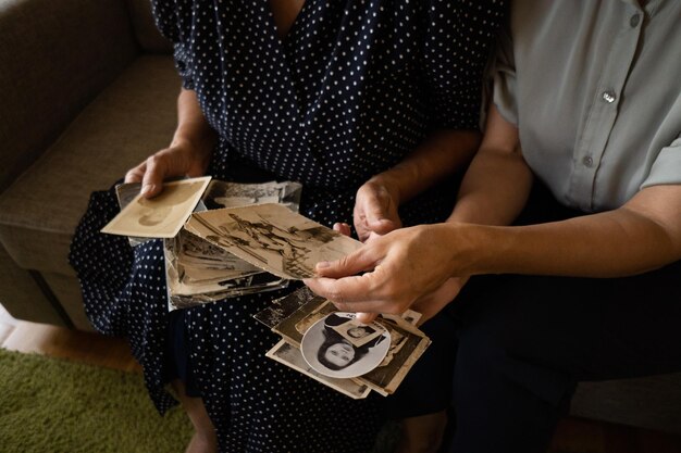 Sección media de una mujer sosteniendo fotos viejas mientras está sentada en el suelo.