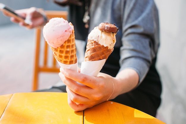 Sección media de una mujer sosteniendo helados en waffles mientras envía mensajes de texto en un restaurante