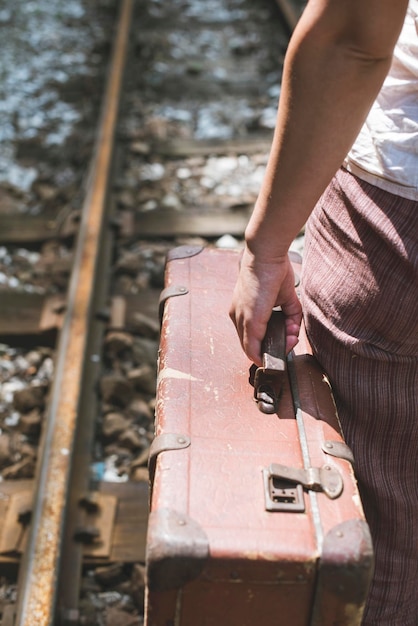 Foto sección media de una mujer sosteniendo una maleta mientras está de pie en la vía del ferrocarril